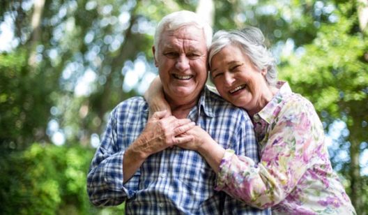 Happy senior woman embracing from behind husband against trees i