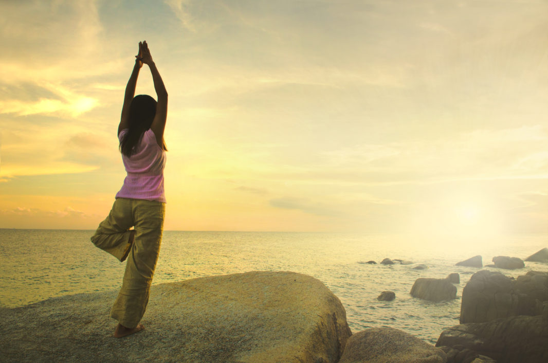 Silhouette young woman practicing yoga on the beach at sunset.